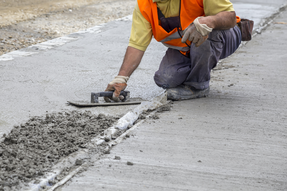 A worker is resurfacing concrete sidewalk using Trowels
